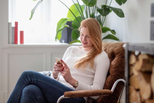 Kvinne sitter i lenestol og ser på mobilen sin