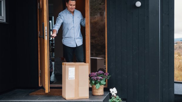 Mann åpner inngangsdøra og ser at det er levert en pakke til ham