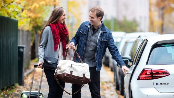 Et smilende par med en bag og en trillekoffert utenfor en bil