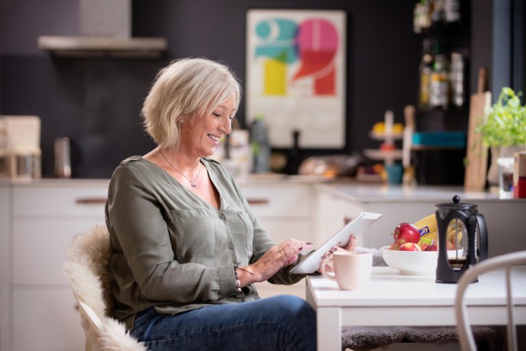 Dame med nettbrett hjemme ved kjøkkenbordet