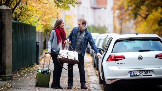 A couple with a suitcase and a bag outside a car