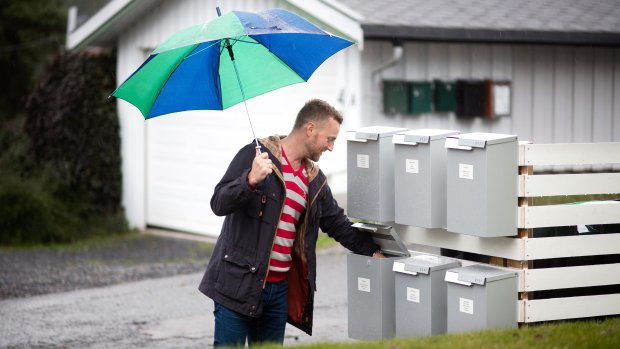 Man with umbrella collects mail from mailbox placed together with several mailboxes.