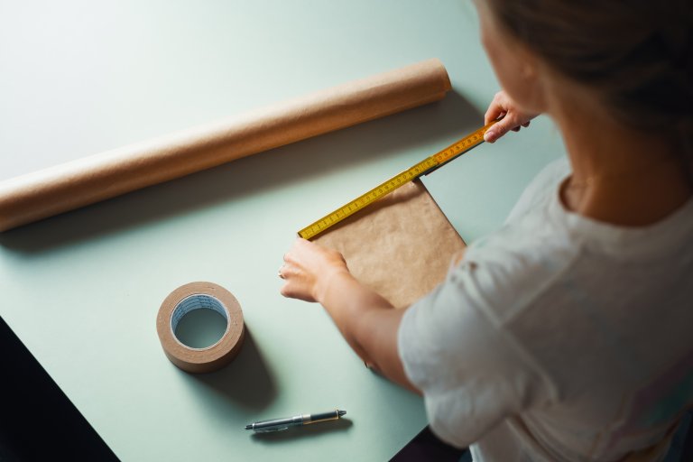 Wrapping paper and tape on the table, and a person is peasuring a letter with a yardstick