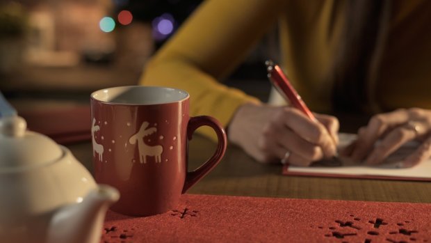 Close up of at tea cup, tea kettle and a hand with a pencil writing a card