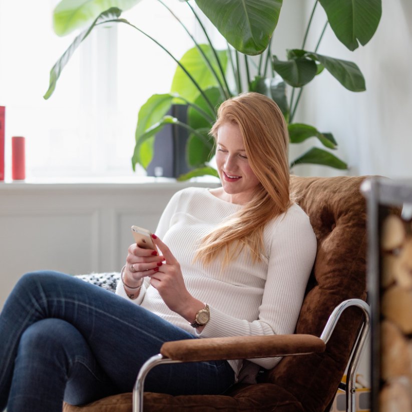 Kvinne sitter i lenestol og ser på mobilen sin