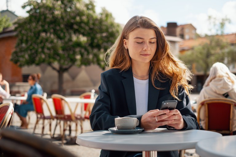 Kvinne på utekafe, ser på mobilen sin