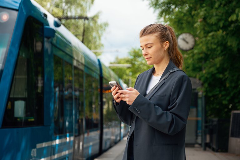 Ung kvinne med mobil venter på trikk