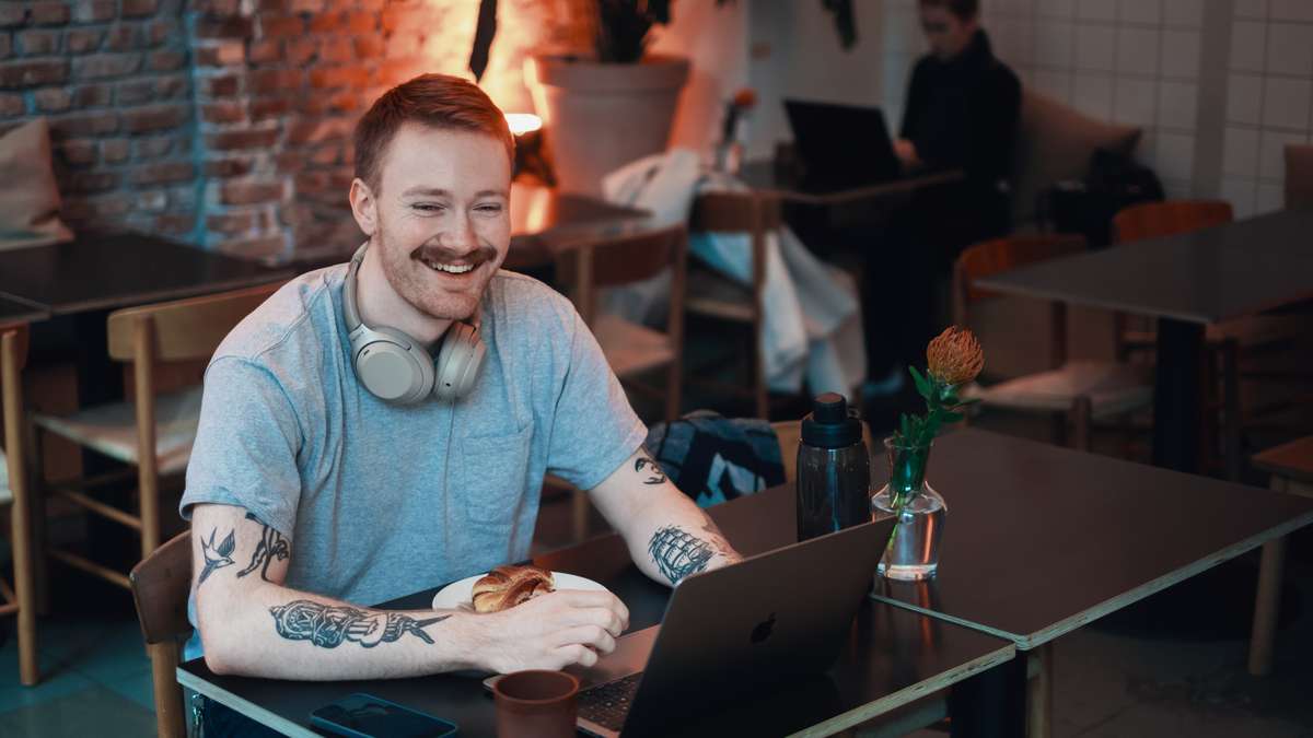 Ung mann smilende på kafe, med høretelefoner og pc
