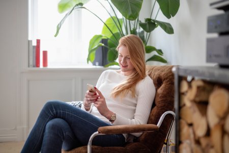 Kvinne sitter i lenestol og ser på mobilen sin