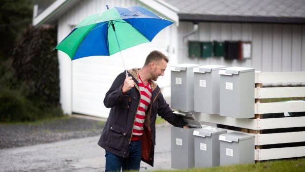 Mann med paraply henter post i postkasse plassert sammen med flere postkasser.