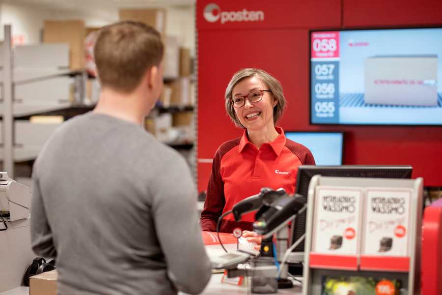 Smilende ansatt på Posten i samtale med en kunde