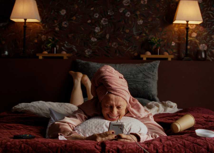 Eldre dame ligger oppå sengen og prater i mobiltelefonen